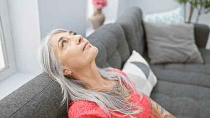 Beautiful middle age woman, with a serious expression innocently settles into her cozy living room...