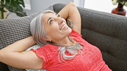 Naklejka premium Middle age grey-haired woman relaxed with hands on head sitting on sofa at home