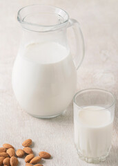 Alternative milk of almonds in a glass and glass jug on a wooden background. copy space