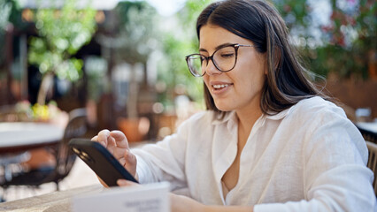 Young beautiful hispanic woman smiling happy using smartphone sitting on the table at bar terrace