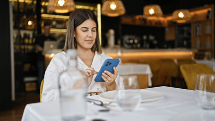 Young beautiful hispanic woman smiling happy using smartphone sitting on the table at the restaurant