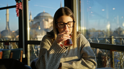 Young woman enjoying tea in a turkish restaurant with a view of the hagia sophia in istanbul.