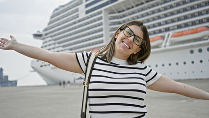 A happy woman with glasses smiles while standing in front of a cruise ship, suggesting vacation and luxury travel.