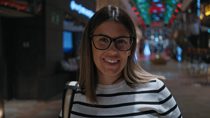 Smiling brunette woman with glasses on a luxury cruise ship interior, illuminated by colorful...