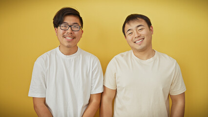 Two asian men smiling in casual attire against a yellow background, portraying friendship or...