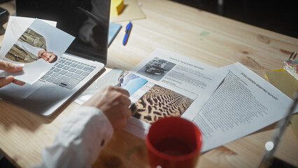 An asian man analyzes photographs and reports in a detective's office, suggesting investigation and evidence assessment.