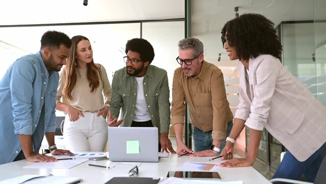 A cheerful group of diverse coworkers lean in around a laptop, indicative of an interactive tech discussion and the high spirits characteristic of a productive and forward-thinking team.