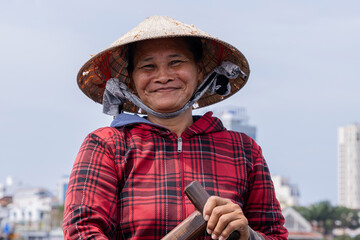 Portrait of an older Vietnamese woman with conical hat, she is looking at the camera while having...