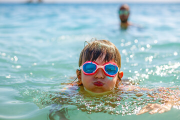 Little girl wearing goggles, swimming in the warm blue sea