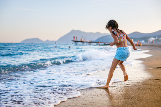 Little girl having fun at the beach, splashing in the water and waves, enjoying a relaxing leisure activity