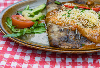Closeup of tasty potato pancake stuffed with pork or beef in spicy saute, cheese sauce. Dinner in the restaurant. Dining out. Table Outside on the street. White-red checkered tablecloth.