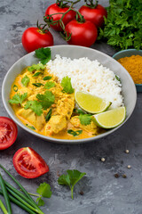 Curry sauce with chicken and rice in a plate, lime, tomatoes, spices and herbs on a dark background. Traditional Indian dish.