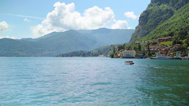 Boat riding off on Lake como Italy with tree covered mountains and clouds