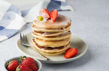 A stack of pancakes with strawberries and a chamomile flower, drizzled with icing on a plate, horizontal..