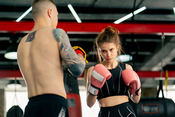 in a boxing fight club a young girl in a black sweatshirt with pink gloves practices with a trainer...