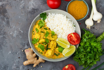 Curry sauce with chicken and rice in a plate, lime, tomatoes, spices and herbs on a dark background, top view, horizontal. Traditional Indian dish.
