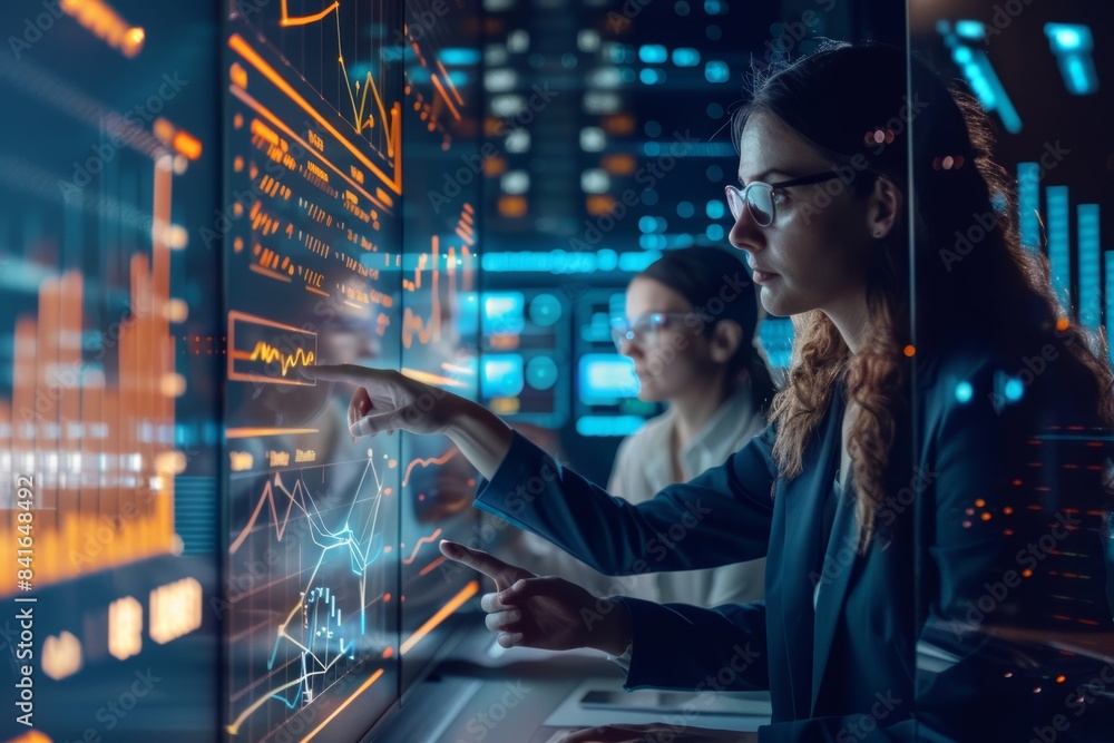 Poster team of business analysts examining data on multiple screens in modern office environment