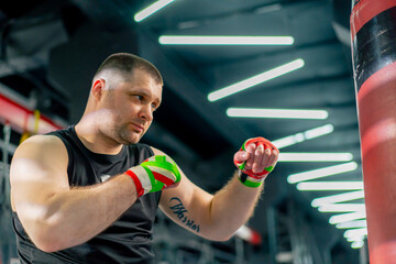 in a boxing fight club senior muscular trainer in a black T-shirt and with multi-colored bandages...