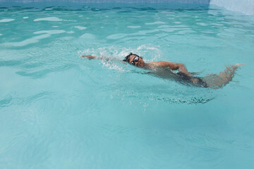 A man wearing swimming goggles swims in the pool in the morning