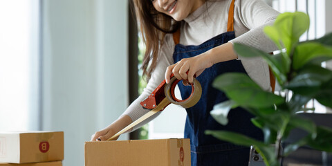 Young business entrepreneur sealing a box with tape. Preparing for shipping, Packing, online...