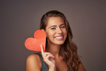Portrait, smile and woman with paper heart in studio for romance, support or care isolated on background. Face, happy and model with love sign for valentines day, kindness or emoji for social media