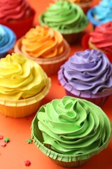 Delicious bright cupcakes and sprinkles on coral background, closeup