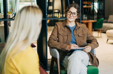 A professional female psychological consultant listens to a client while sitting at her workplace.