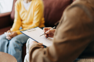 Close-up of a psychologist's hands writing down notes about a patient in a notebook. The psychologist makes a social survey of the reference group. A professional is talking to a client.