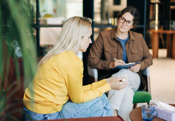 Psychologist writing down notes about a patient in a notebook. The psychologist makes a social survey of the reference group. A professional is talking to a client. © Ilona