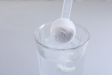Adding baking soda into glass of water on light grey background, closeup