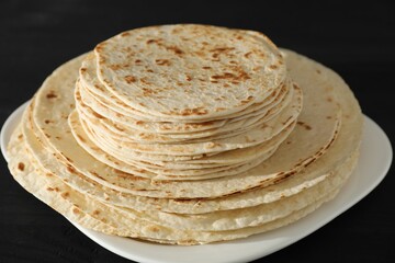 Many tasty homemade tortillas on black wooden table, closeup