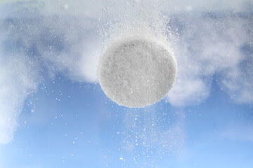 Effervescent pill dissolving in water on light blue background, closeup