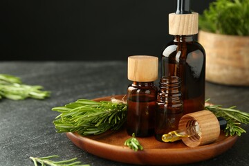 Essential oils in bottles and rosemary on gray table, closeup. Space for text