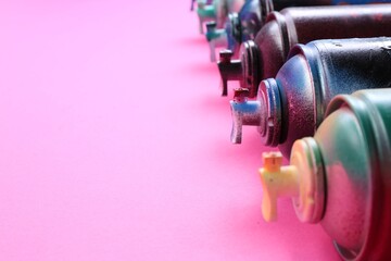 Many spray paint cans on pink background, closeup. Space for text