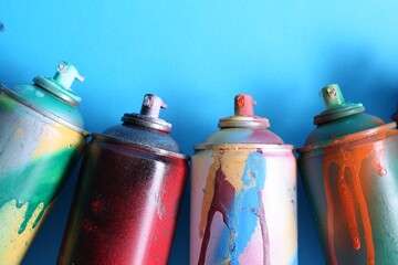 Many spray paint cans on light blue background, flat lay