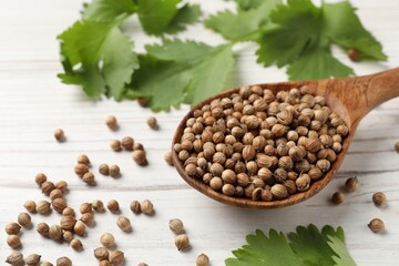 Spoon with dried coriander seeds and green leaves on wooden table, closeup