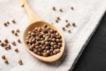 Spoon with dried coriander seeds and light cloth on dark gray table, closeup