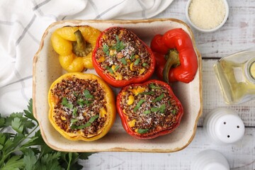 Tasty quinoa stuffed bell peppers with corn in baking dish on white wooden table, flat lay
