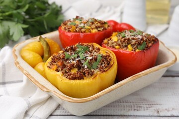 Tasty quinoa stuffed bell peppers with corn in baking dish on white wooden table, closeup
