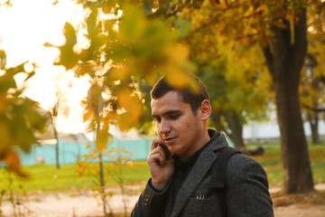 Obraz premium Man talking on the phone outdoors in autumn. Mobile communication: man talking on his phone in a casual autumn scene