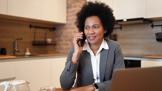African American businesswoman working on her laptop from home and talking on mobile phone