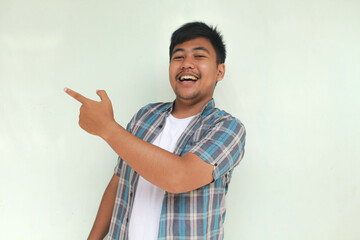 Smiling and happy Asian man pointing finger to empty space beside him isolated gray background.