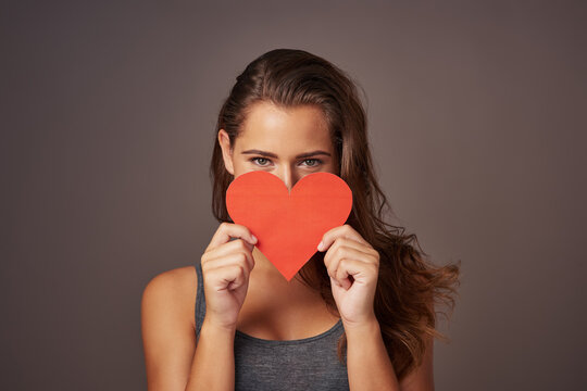 Portrait, love and woman with paper heart in studio for romance, support or donate isolated on background. Face, care or model with sign for valentines day, kindness or hide on emoji for social media - Powered by Adobe