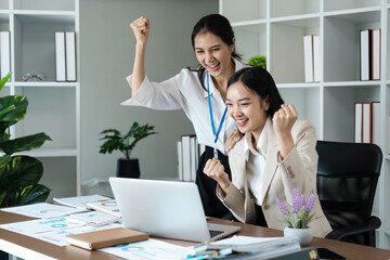 Two women are celebrating in a cubicle with a laptop on the desk