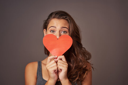 Portrait, love and woman with paper heart in studio for romance, support or donation isolated on background. Face, care and model with sign for valentines day, kindness or hide on social media emoji