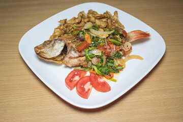 Indonesian food: fried nile tilapia (ikan nila goreng) with stir fried bok choy (sawi), crispy fried oyster mushroom (jamur tiram), and chopped tomatoes; on top of white rectangular plate