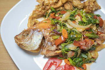 Indonesian food: fried nile tilapia (ikan nila goreng) with stir fried bok choy (sawi), crispy fried oyster mushroom (jamur tiram), and chopped tomatoes; on top of white rectangular plate