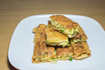 Indonesian food: Martabak Telur (omelette murtabak/mutabbak/matabbak/mutabbaq), which is a folded omelette pancake with bits of vegetables, on top of white rectangular plate, on top of wooden table