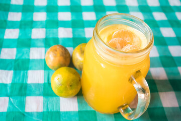 Mandarin orange juice in a glass, with three mandarin oranges, on top of a checkered tablecloth