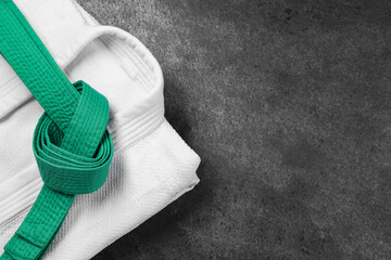 Green karate belt and white kimono on gray textured background, top view. Space for text
